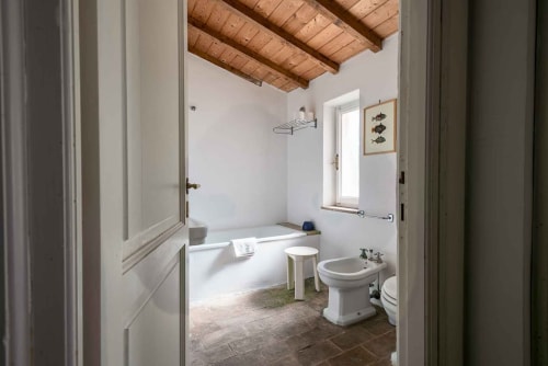 Bagno rustico con travi in legno a vista, vasca, lavandino e pavimento in cotto presso Donkeys & Roses a Viterbo
