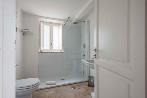 Bagno moderno con box doccia in vetro, lavabo bianco, toilette e finestra nell'appartamento Donkeys & Roses a Viterbo