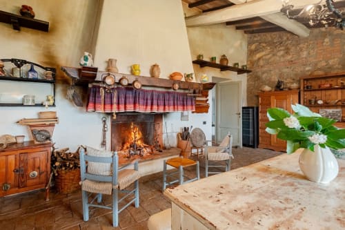 Cucina rustica in stile casale con camino a legna, travi a vista, arredi tradizionali e fiori bianchi in vaso