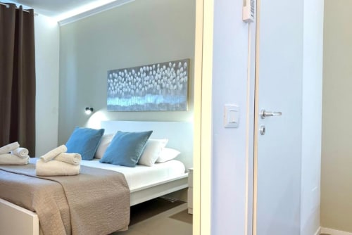 Camera da letto moderna nell'appartamento di Palermo con cuscini blu, biancheria bianca, asciugamani arrotolati e opera d'arte astratta sopra il letto