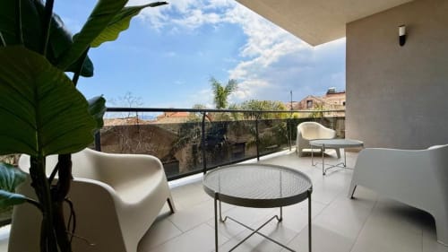 Terrazza moderna dell'appartamento di Palermo con sedie bianche, tavolo rotondo, vista sul mare e vegetazione rigogliosa
