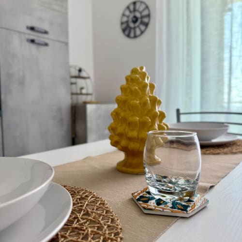 Tavolo da pranzo in moderno appartamento a Palermo con bicchiere d'acqua, pigna decorativa gialla, stoviglie bianche e vista sulla cucina