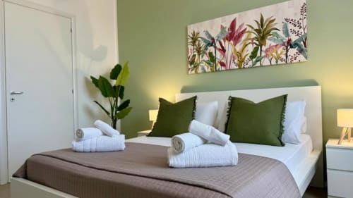Camera da letto moderna a Palermo con parete accent verde, letto bianco, cuscini verdi, piante fresche e decorazioni botaniche colorate