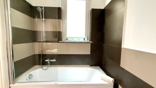 Bagno moderno con piastrelle a righe, vasca bianca e cabina doccia in vetro nell'appartamento di Palermo