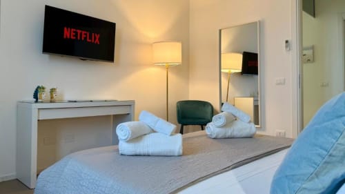 Camera da letto moderna con TV Netflix, scrivania, specchio, lampada da terra e asciugamani arrotolati sul letto in appartamento a Palermo con vista mare