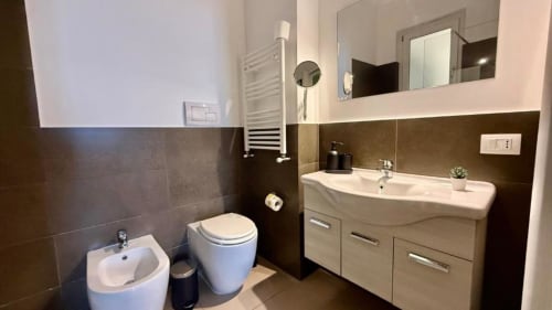 Bagno moderno in appartamento a Palermo con piastrelle marroni, lavabo bianco, WC, bidet e scaldasalviette