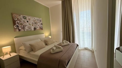 Camera da letto moderna a Palermo con pareti verdi, letto bianco, biancheria marrone, arte astratta e accesso alla terrazza
