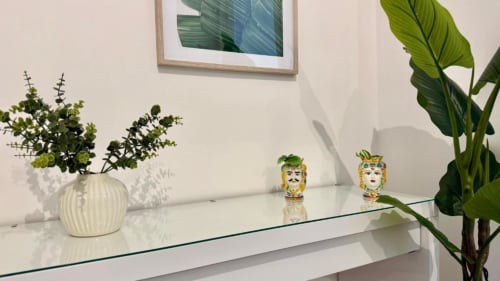 Interno minimalista di appartamento a Palermo con piante in vaso, sculture decorative di volti e ripiano in vetro con vista sul mare