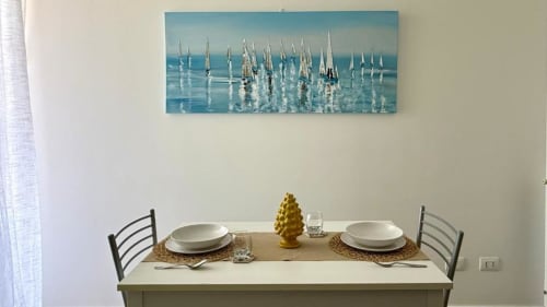 Tavolo da pranzo apparecchiato per due con opera d'arte marina nella residenza palermitana, piatti bianchi e decorazioni dorate.