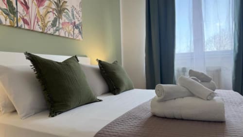 Camera da letto dell'appartamento a Palermo con cuscini verdi, biancheria bianca, asciugamani freschi, opere d'arte floreale e vista sul mare