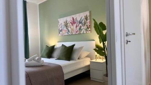 Camera da letto moderna in appartamento a Palermo con parete verde, letto bianco, opere botaniche e pianta in vaso