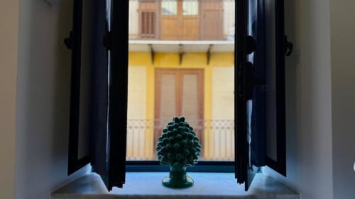 Porte nere aperte incorniciano una decorazione di ananas verde che affaccia su un cortile giallo di Palermo in questo appartamento siciliano