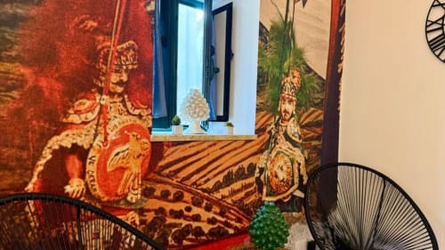 Interno di appartamento a Palermo con arazzi asiatici ornati, finestra con cornice blu, sedie in filo nero e decorazioni di cactus verde