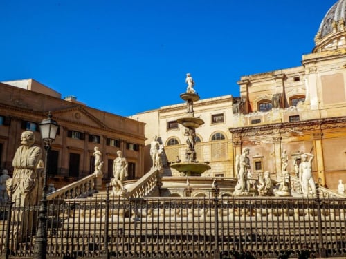La storica Piazza Pretoria di Palermo con edifici barocchi, fontana e statue sotto un cielo azzurro limpido
