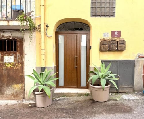 Ingresso di appartamento a Palermo con facciata gialla, porta in legno e piante in vaso in edificio storico italiano