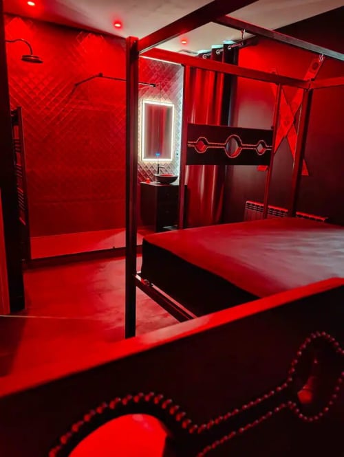 Modern luxury bedroom with red ambient lighting, canopy bed, and contemporary bathroom at La Maison Defendue hotel in