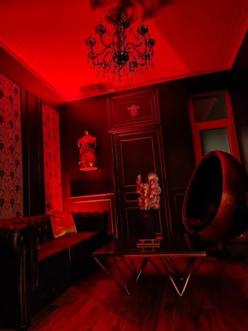 Red neon-lit lounge room at La Maison Defendue hotel in Tessy-Bocage with chandelier and modern furnishings