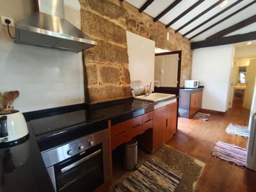 Cozinha moderna com parede de acentuação em pedra, eletrodomésticos em aço inoxidável e armários em madeira na villa SM Stays, Guarda Portugal