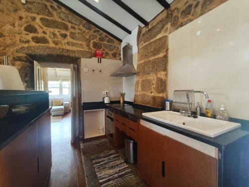 Cozinha moderna da coleção SM Stays, Guarda PT, com paredes de pedra, bancadas escuras e eletrodomésticos em aço inoxidável