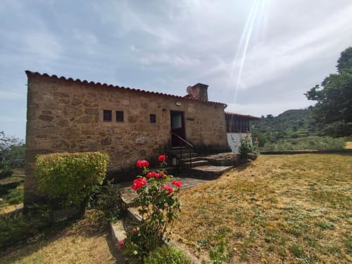 Vila rústica de pedra com flores vermelhas em jardim de Guarda, Portugal, cercado por colinas verdejantes