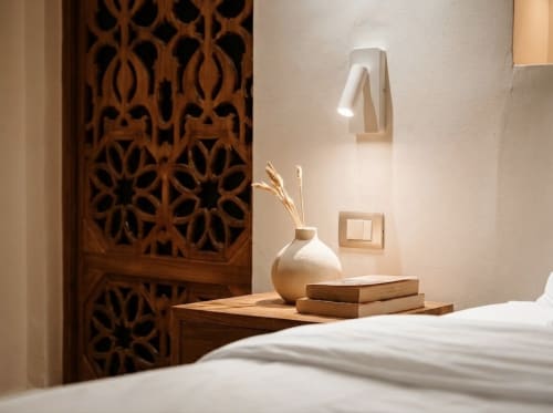 Dormitorio minimalista en Villa Merida Boutique Hotel con biombo de madera tallada, lámpara de pared blanca, jarrón decorativo y libros