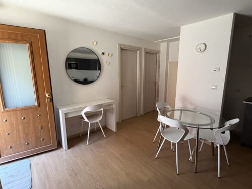 Monolocale moderno nel centro di Verona con scrivania bianca, specchio rotondo, tavolo da pranzo e pavimenti in legno