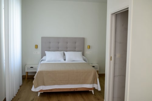 Moderna habitación del Hotel Boutique Alcazaba Salobrena con cabecero tapizado gris, mesillas blancas y vista al jardín