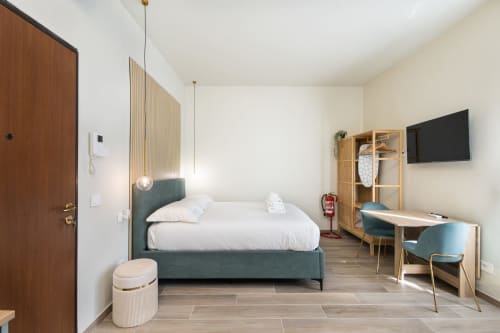 Modernes Schlafzimmer in den Magnolia Apartments Mailand mit Türkisbett, Holzschreibtisch, Wandfernseher und minimalistischer Einrichtung