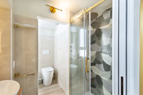Modernes Badezimmer in den Magnolia Apartments Mailand mit Glasdusche, weißem WC, Fliesen mit Blattmuster und Messingausstattung