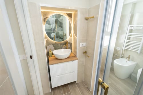 Modernes Badezimmer in den Magnolia Apartments Milan mit rundem beleuchteten Spiegel, weißem Aufsatzwaschbecken, Holzwaschtisc und Glas