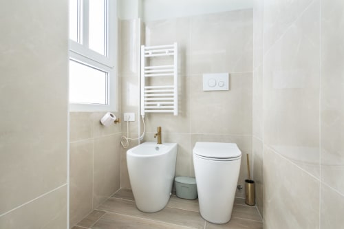 Modernes Badezimmer in den Magnolia Apartments Mailand mit weißem Bidet, Toilette, Handtuchhalter und gekachelten Wänden mit natürlichem Licht