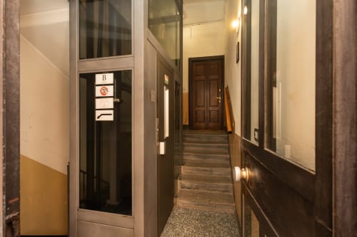 Moderner Flur im Magnolia Apartments Mailand mit dunklen Wänden, Holztreppe und beleuchtete Eingangstür markiert 'B'