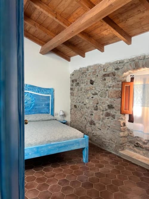 Camera da letto rustica in pietra con letto dipinto di blu, soffitto con travi in legno e pavimento in cotto a Regnos Altos, Bosa, Italia