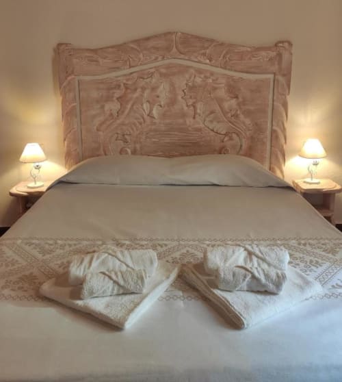 Camera da letto elegantemente decorata a Regnos Altos Boutique Rooms a Bosa con testata in legno intagliato, asciugamani bianchi e comodino