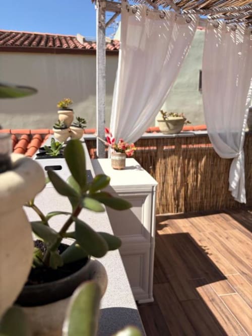 Terrazza soleggiata a Regnos Altos con succulente in vaso, pergolato bianco e vista sui tetti in terracotta di Bosa