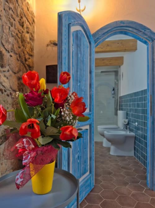 Tulipani rossi in vaso giallo all'ingresso dell'arco blu del bagno di Regnos Altos Boutique Rooms a Bosa, Italia