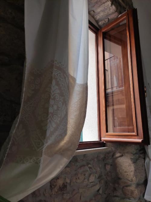 Finestra in legno con tenda trasparente in camera in pietra storica presso Regnos Altos Boutique, Bosa