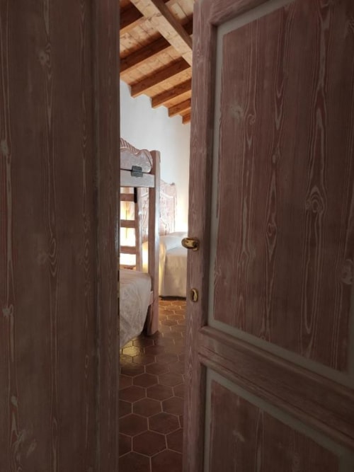 Porte in legno scuro che si aprono sulla camera da letto con travi in legno a vista presso Regnos Altos Boutique Rooms a Bosa, Italia
