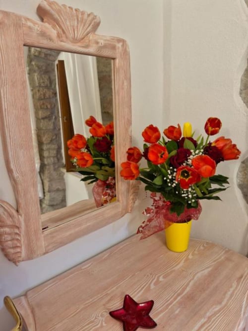 Elegante camera a Regnos Altos Boutique Rooms a Bosa con bouquet di tulipani rossi, specchio in legno e arredamento rustico