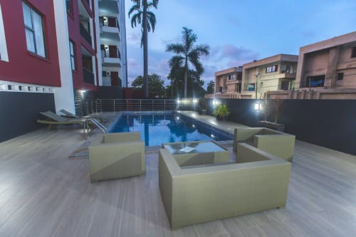 Cozy Apartments Ghana pool area at dusk with modern seating, illuminated blue water, and surrounding residential buildings in