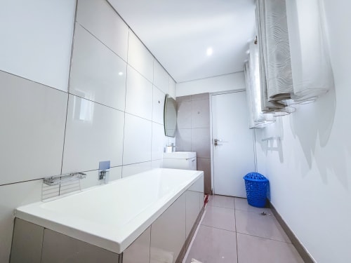 Modern bathroom in Ridge Apartment at Cozy Apartments Ghana with white tile vanity, large mirror, and white walls in Accra