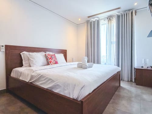 Modern bedroom at Cozy Apartments Ghana Ridge Apartment with wooden bed, white linens, gray curtains, and city view balcony