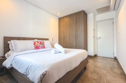 Modern bedroom at Cozy Apartments Ghana with king bed, wood wardrobe, white door, and wooden flooring in Accra