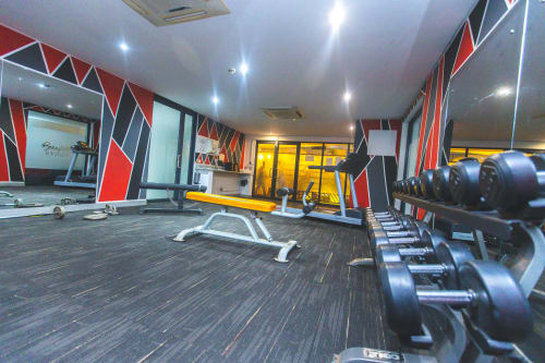 Modern gym facility at Cozy Apartments Ghana with dumbbells, workout bench, and red accent wall décor in Accra