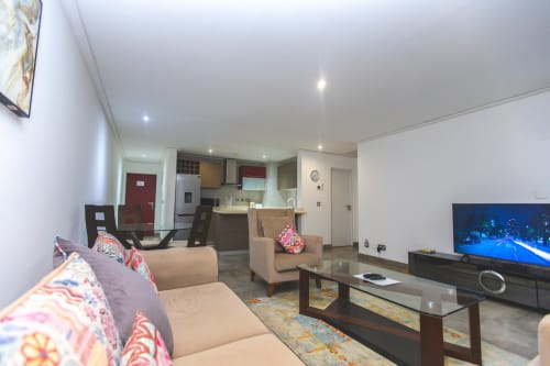 Modern open-plan living area in Ridge Apartment at Cozy Apartments Ghana with beige sofa, 50-inch TV, kitchenette, and