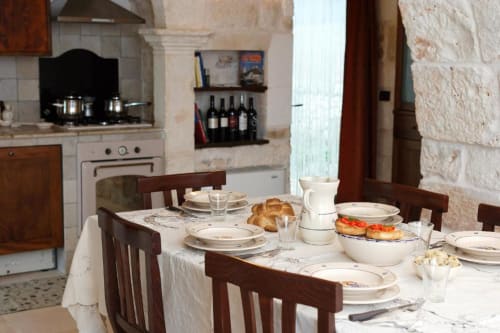 Tavolo da colazione apparecchiato a Trulli Boccadoro con pasticcini, frutta e caffè in una rustichezza cucina italiana.