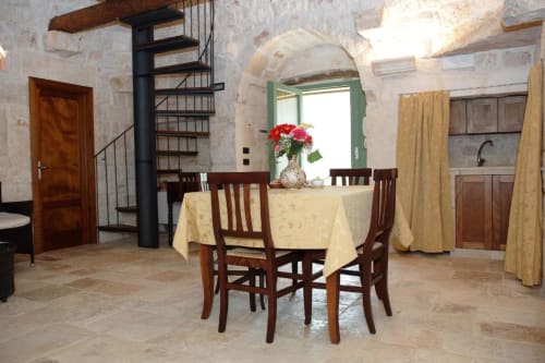 Zona pranzo nell'appartamento Studio Trullo a Trulli Boccadoro con tavolo rotondo, sedie in legno, muri in pietra ad arco e scala a spirale