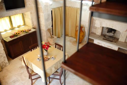 Monolocale Trulli Boccadoro: zona pranzo con tavolo, camino, cucina e caratteristica architettura in pietra
