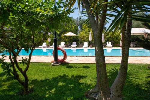 Giardino Trulli Boccadoro con piscina, lettini, palme e scultura rossa in Puglia