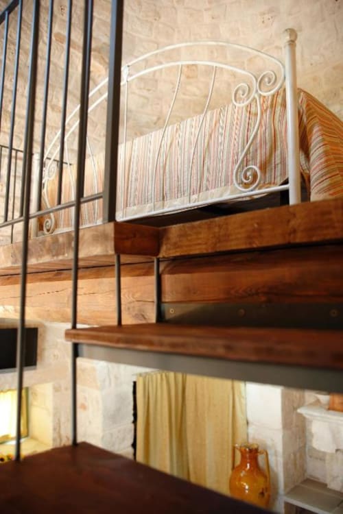 Camera da letto in soppalco con ringhiera in ferro battuto e travi in legno nello studio Trulli Boccadoro, Puglia